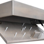 Industrial metal access hatch opened at an angle, showing a sloped interior with white pegs and a hydraulic support arm.