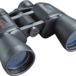Close-up of black binoculars with a central focusing wheel, viewed from the front-right.