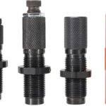 Row of four knurled black metal adapters with threaded shafts next to an orange anodized connector on the right.
