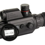 Black tactical riflescope with magnifier attachment and adjustment knobs, shown from the side on a white background.