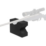 Rifle with scope resting on a black front shooting rest on a white background.