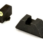 Two black plastic mechanical parts—a small rectangular block with a brass insert, and a larger wedge with a central slot.