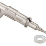 Metal precision nozzle with a tapered tip and a side clamp, labeled APEX, shown alongside a small white circular gasket.