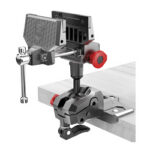 Metal bench vise mounted on a light wood workbench, with a red adjustment knob and a long handle for tightening parts.