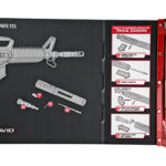 Toy blaster construction kit laid out on a black mat; gray disassembled parts and screws, with step-by-step assembly panels and a clear plastic storage tray on the right.