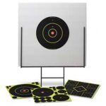 Target practice stand with a large black bullseye target on a sheet, and four paper targets laid on the ground nearby.