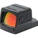 Compact black red-dot sight with orange-tinted window, mounted on a small rail, featuring two side adjustment dials.
